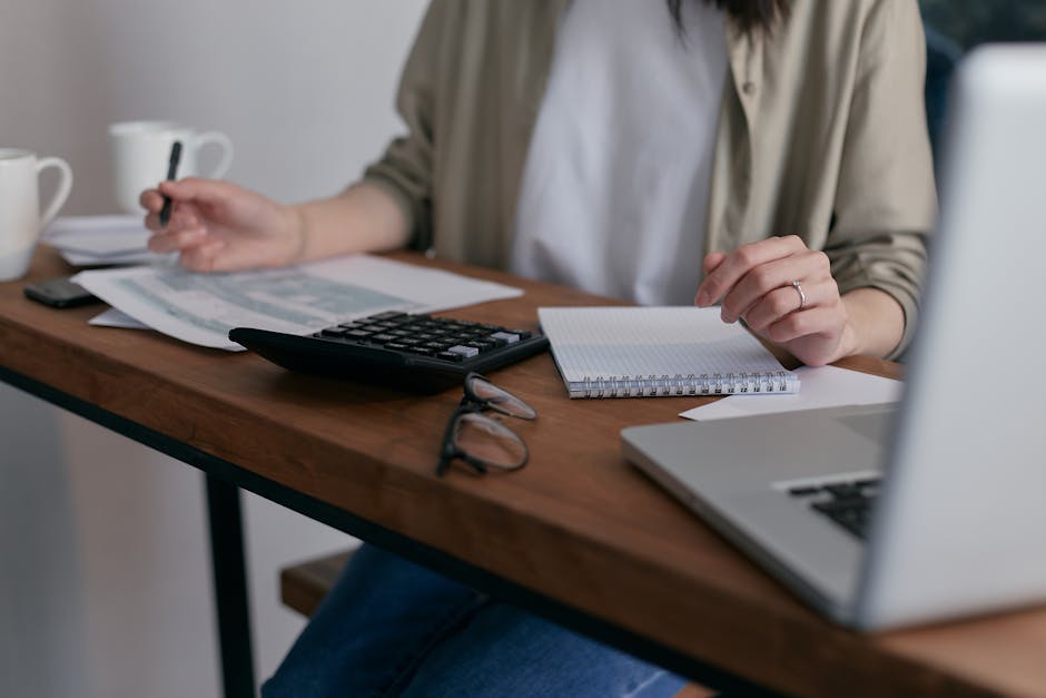 A person sitting at a clean desk, focused on writing in a notebook with a laptop nearby.